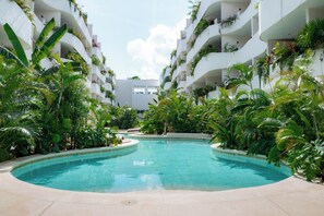 A pool surrounded by lush greenery and white buildings with balconies. - Vrbo Property (Tulum)