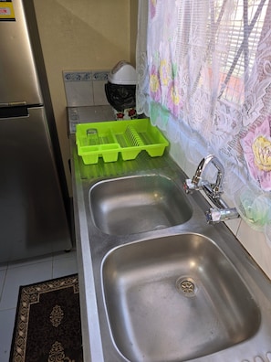 A kitchen with stainless steel sinks, a green dish rack, and a refrigerator.