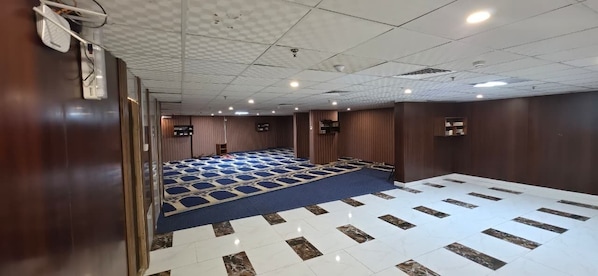 A conference room with a blue carpet, white and brown patterned floor, wooden walls, and ceiling-mounted lights.