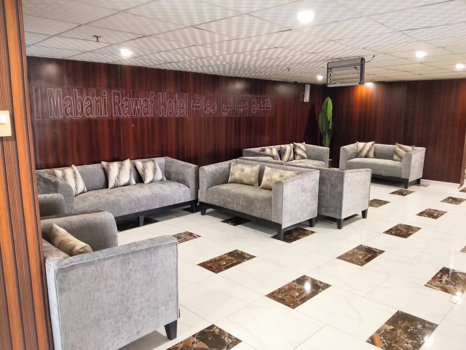 A lobby with grey sofas and armchairs, a wooden wall with a sign, and a tiled floor with marble accents.