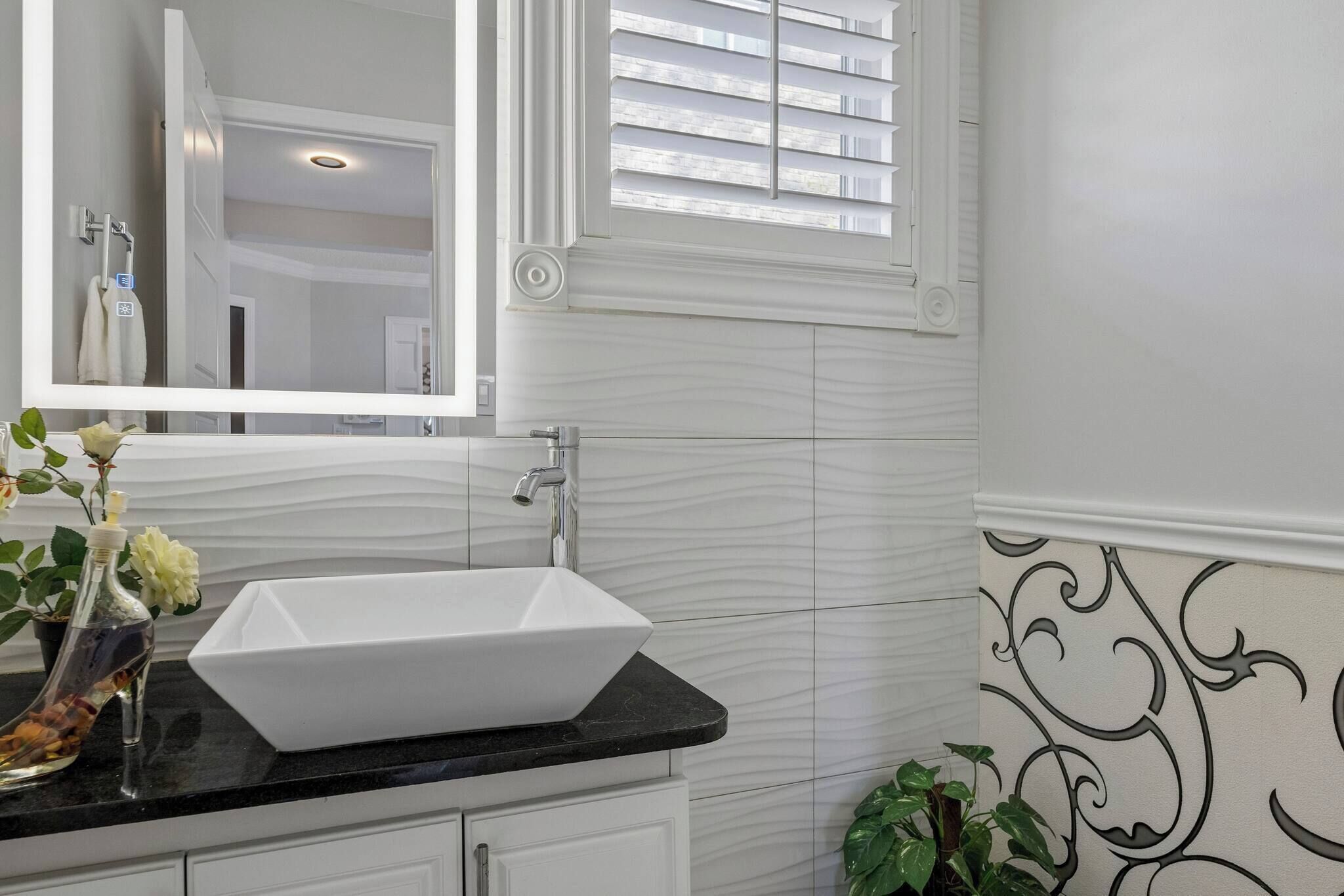 A bathroom with a white vanity, a vessel sink, a mirror, and a window with blinds.