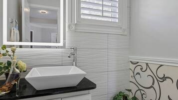 A bathroom with a white vanity, a vessel sink, a mirror, and a window with blinds.