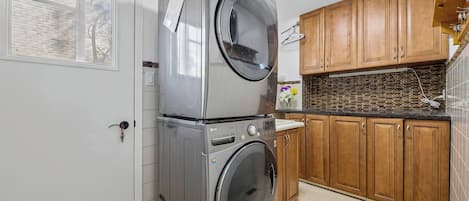 A laundry area with stacked washers and dryers, wooden cabinets, and a tiled backsplash.