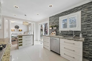 A modern kitchen with a central island, white cabinetry, and a backsplash with grey tiles.