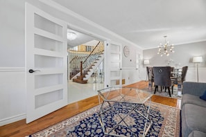 A spacious living room with a staircase, a dining area, and a chandelier.