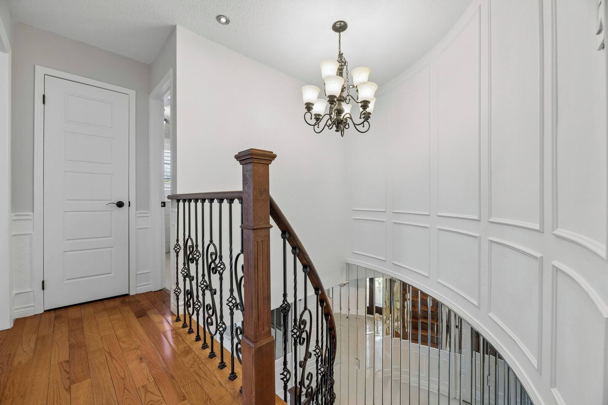 Un escalier avec une main courante en bois et des balustres noires, menant à un palier où se trouve une porte blanche.