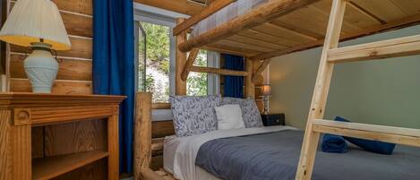 A bunk bed room with a wooden desk and a lamp.