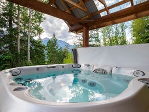 Ein Whirlpool unter einer hölzernen Pergola, umgeben von Bäumen und Bergen im Hintergrund.