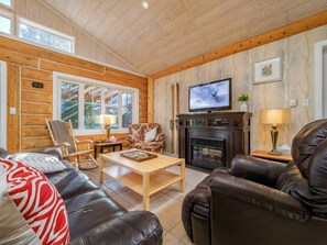 Ein gemütliches Wohnzimmer mit Kamin, Ledersofas, einem Holztisch und einem Fernseher.