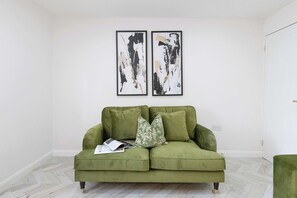 A green sofa with floral cushions, a magazine, and two abstract paintings on the wall. - Stylish Home Near Chelsfield Station, Free WiFi (Orpington)