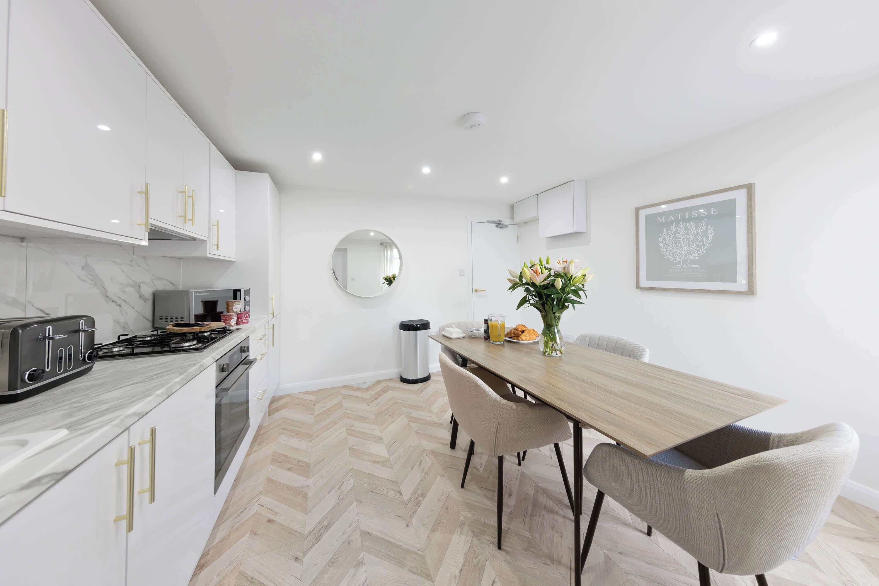 A modern kitchen with white cabinets, a marble countertop, and a dining area with a wooden table and chairs.