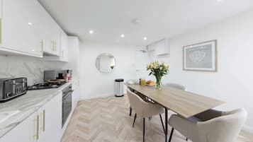 A modern kitchen with white cabinets, a marble countertop, and a dining area with a wooden table and chairs.