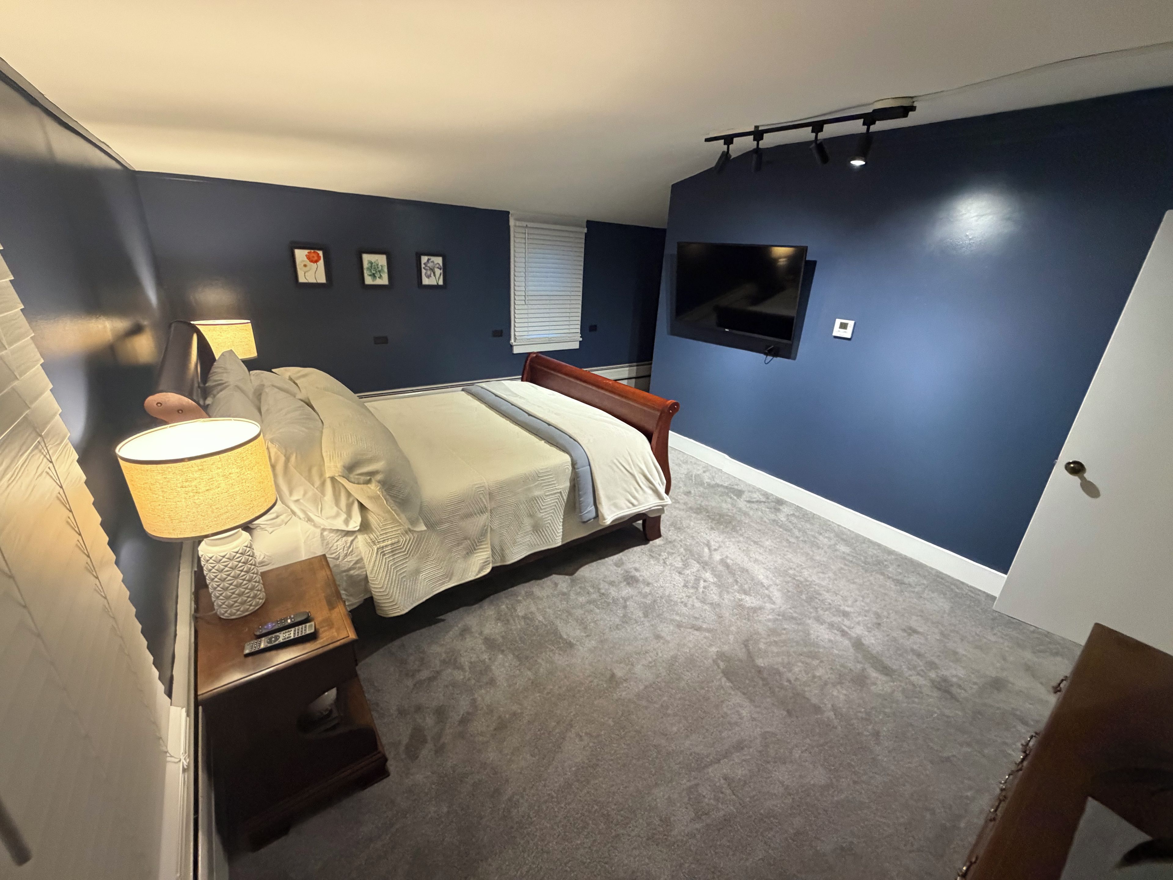 Ein Schlafzimmer mit einem Bett, Nachttischlampen, einem Fernseher und gerahmten Bildern an der Wand.