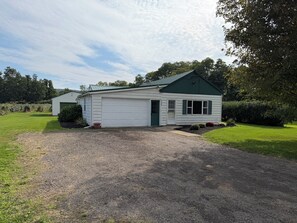 A single-story house with a green roof and white siding, a gravel driveway, and a well-maintained lawn. - West & Vine - Lake Erie Fishing & Wine Country (Ripley)