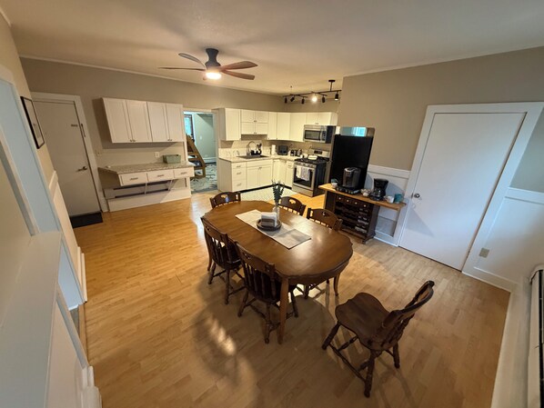 A modern kitchen with white cabinets, a dining area with a wooden table and chairs, and a ceiling fan.
