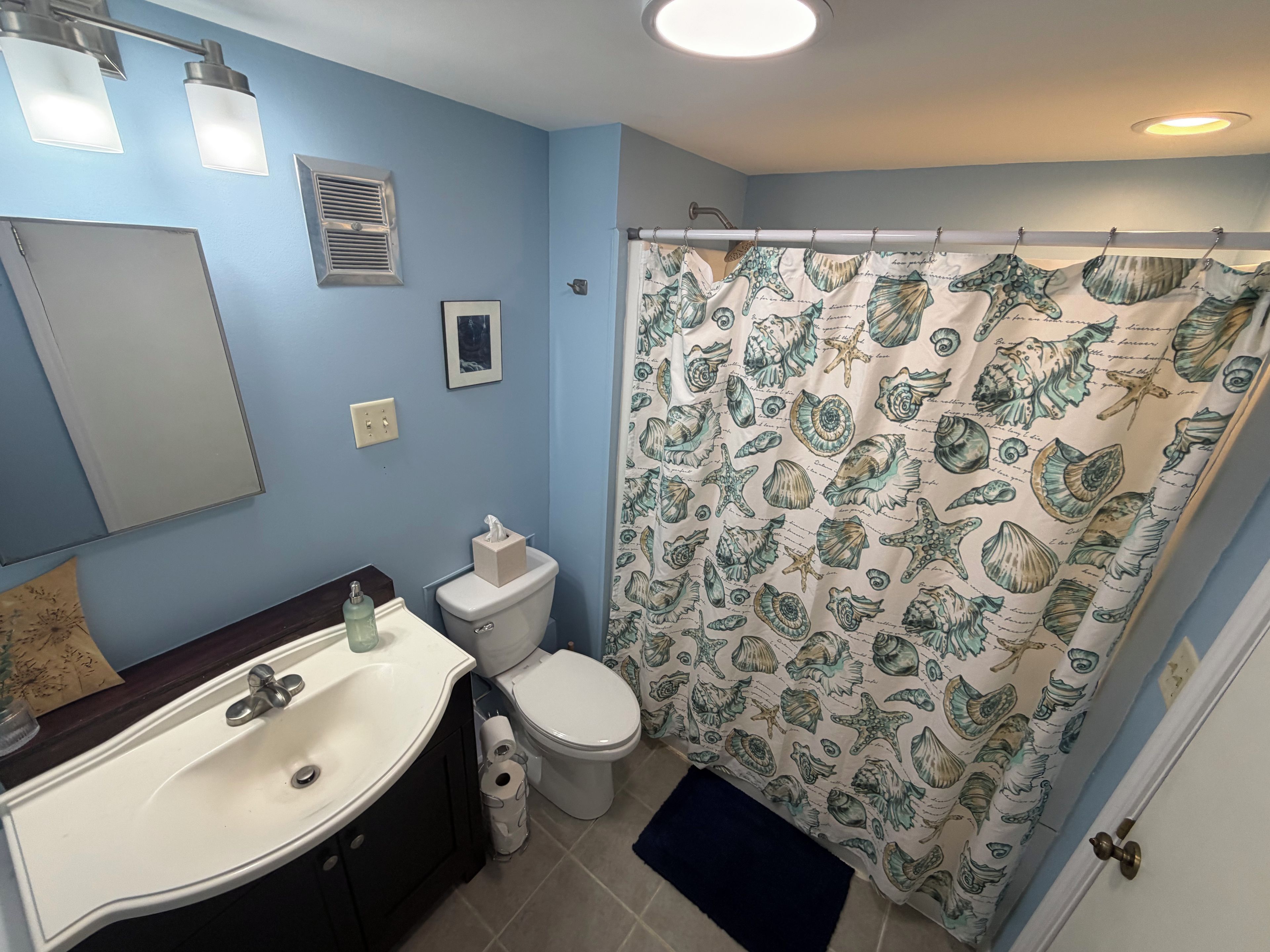 Un baño con lavamanos, inodoro y cortina de ducha con diseño de conchas marinas.