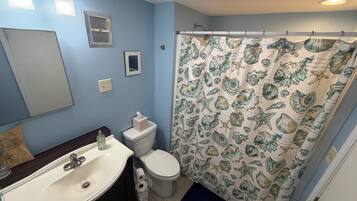 Un baño con lavamanos, inodoro y cortina de ducha con diseño de conchas marinas.