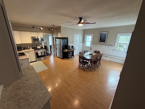 A spacious kitchen with modern appliances, a dining area with wooden chairs, and a ceiling fan.