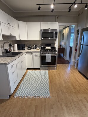 A modern kitchen with white cabinets, stainless steel appliances, a patterned rug, and wooden flooring.