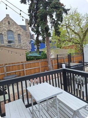 Eine Terrasse mit weiß gestrichenen Holzmöbeln, ein Steinhaus im Hintergrund und ein Holzzaun.