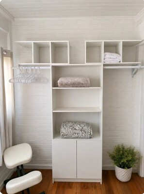 A white closet with multiple shelves and a hanging rod, a white chair, and a potted plant. - Denver Retreat Hot Tub • Game Room • Sleeps 16+ (Denver)