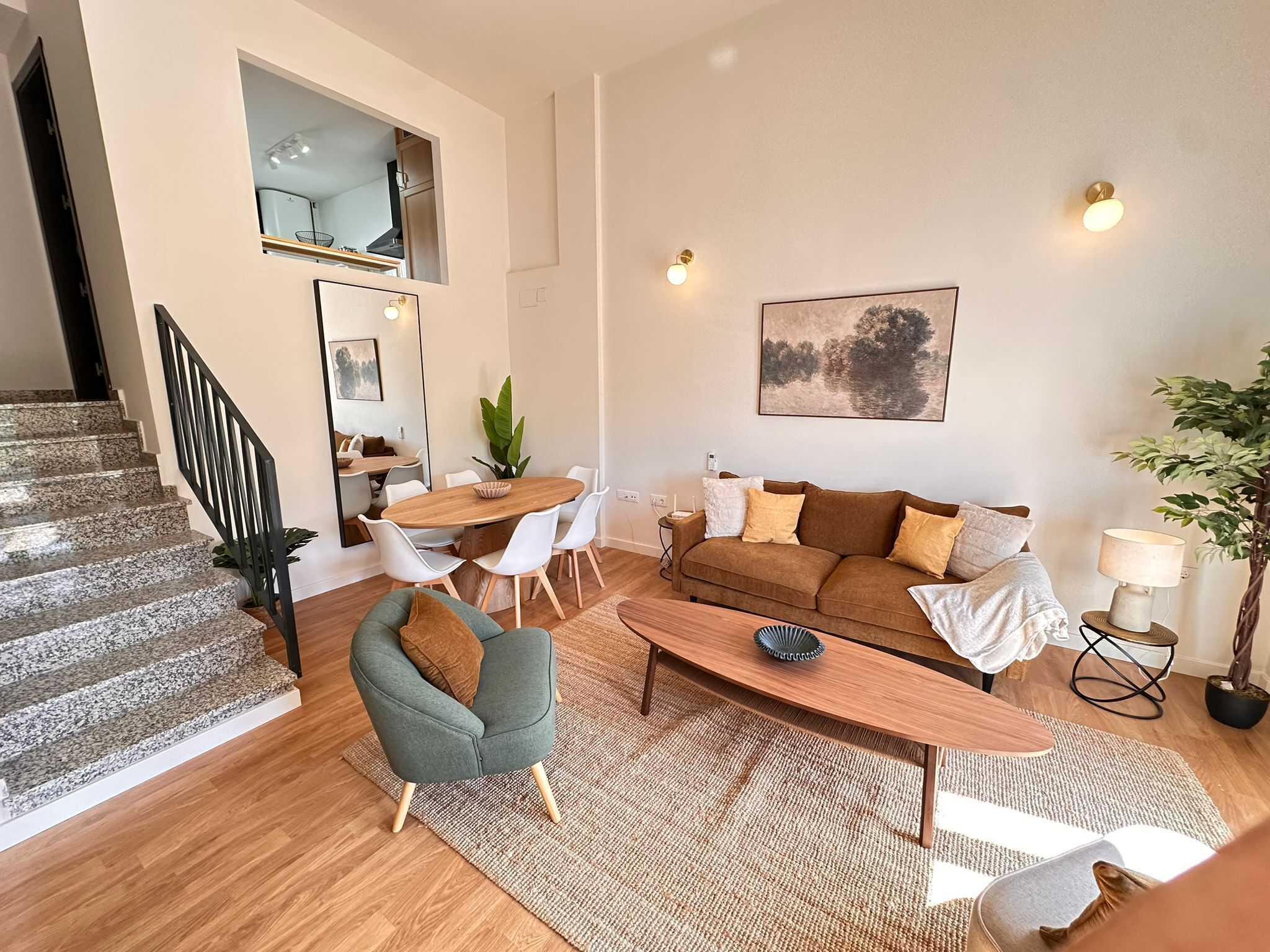 A modern living room with a sofa, coffee table, and chairs, a staircase, and a dining area with a table and chairs.