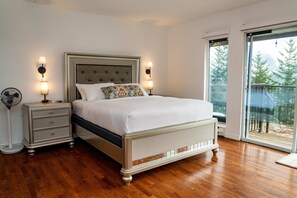 Een slaapkamer met een bed, nachtkastjes, een vloerlamp en uitzicht door een glazen deur.