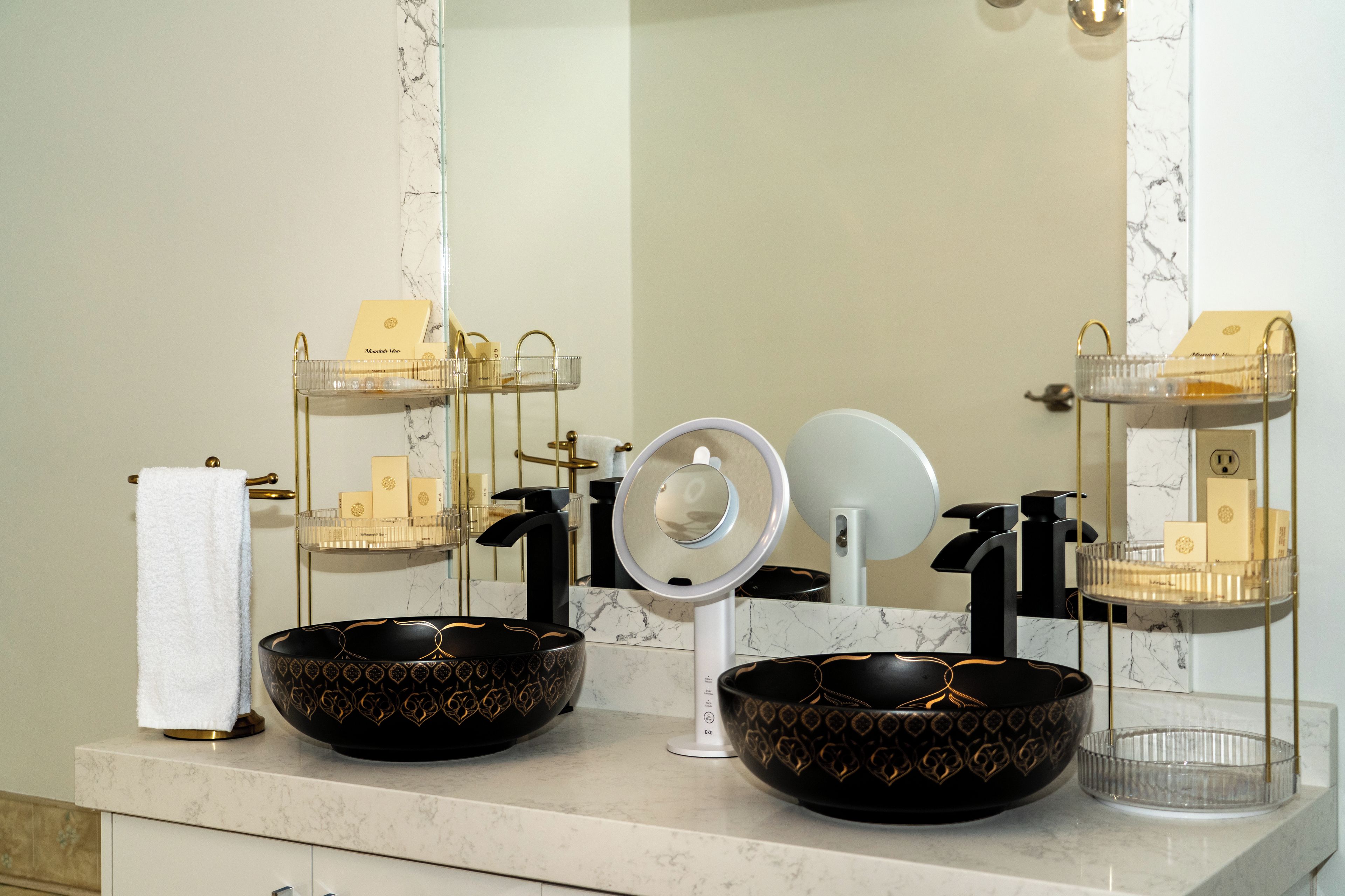 A bathroom with two black bowls with gold patterns, a white towel, and a mirror with a ring light.