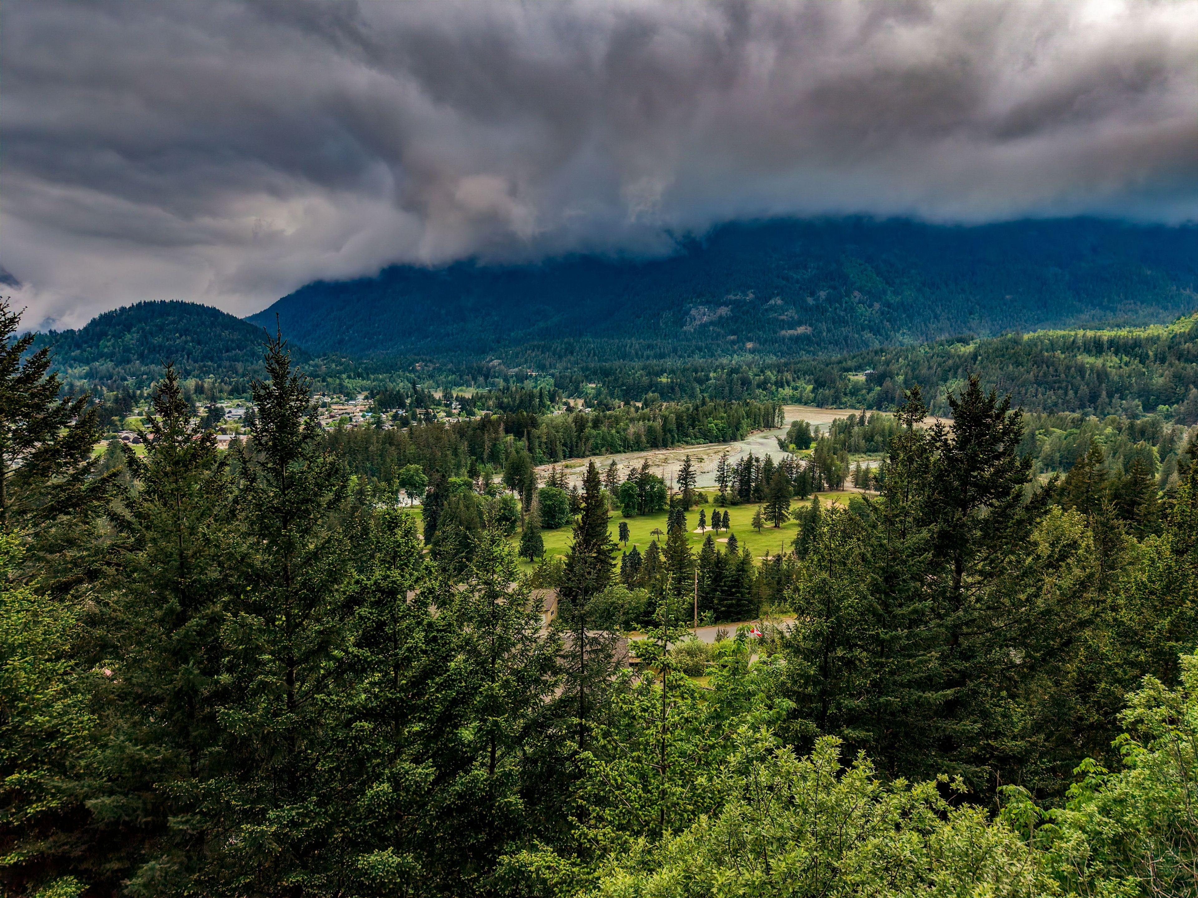 A mountainous landscape with dense forests and a valley with buildings.