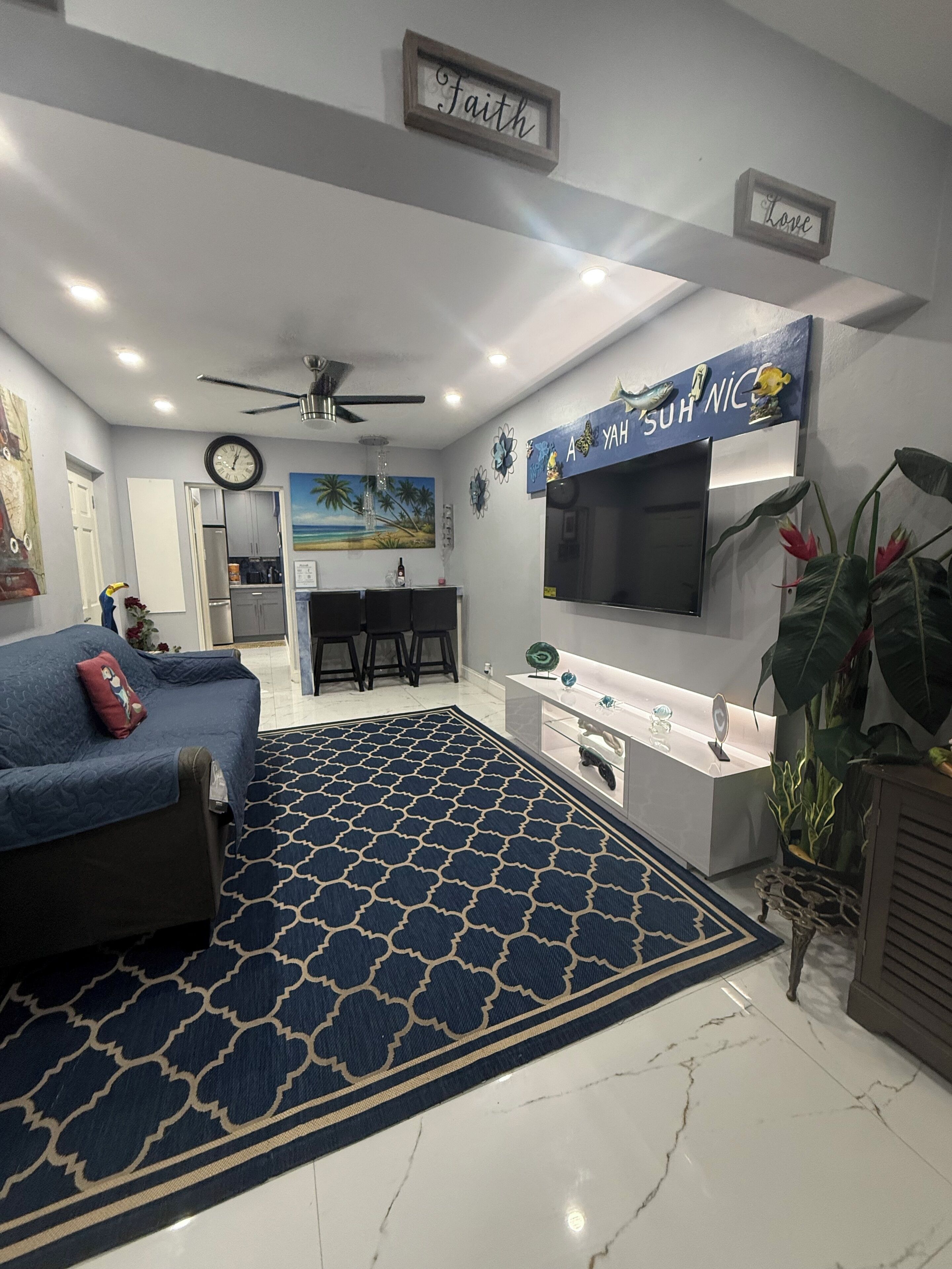 Una sala de estar moderna con un tapete azul estampado, un sofá, un televisor y una cocina con encimera blanca.