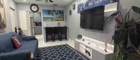 A modern living room with a blue patterned rug, a sofa, a TV, and a kitchen area with a white countertop.
