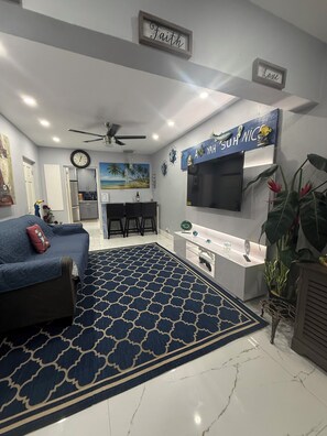 A modern living room with a blue patterned rug, a sofa, a TV, and a kitchen area with a white countertop. -  Beautiful and updated Cozy 2 Bedroom,2 Bathroom inPeaceful Portmore,Sleeps six. (Portmore)