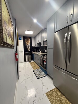 A modern kitchen with stainless steel appliances, a marble floor, and a fire extinguisher on the wall. -  Beautiful and updated Cozy 2 Bedroom,2 Bathroom inPeaceful Portmore,Sleeps six. (Portmore)