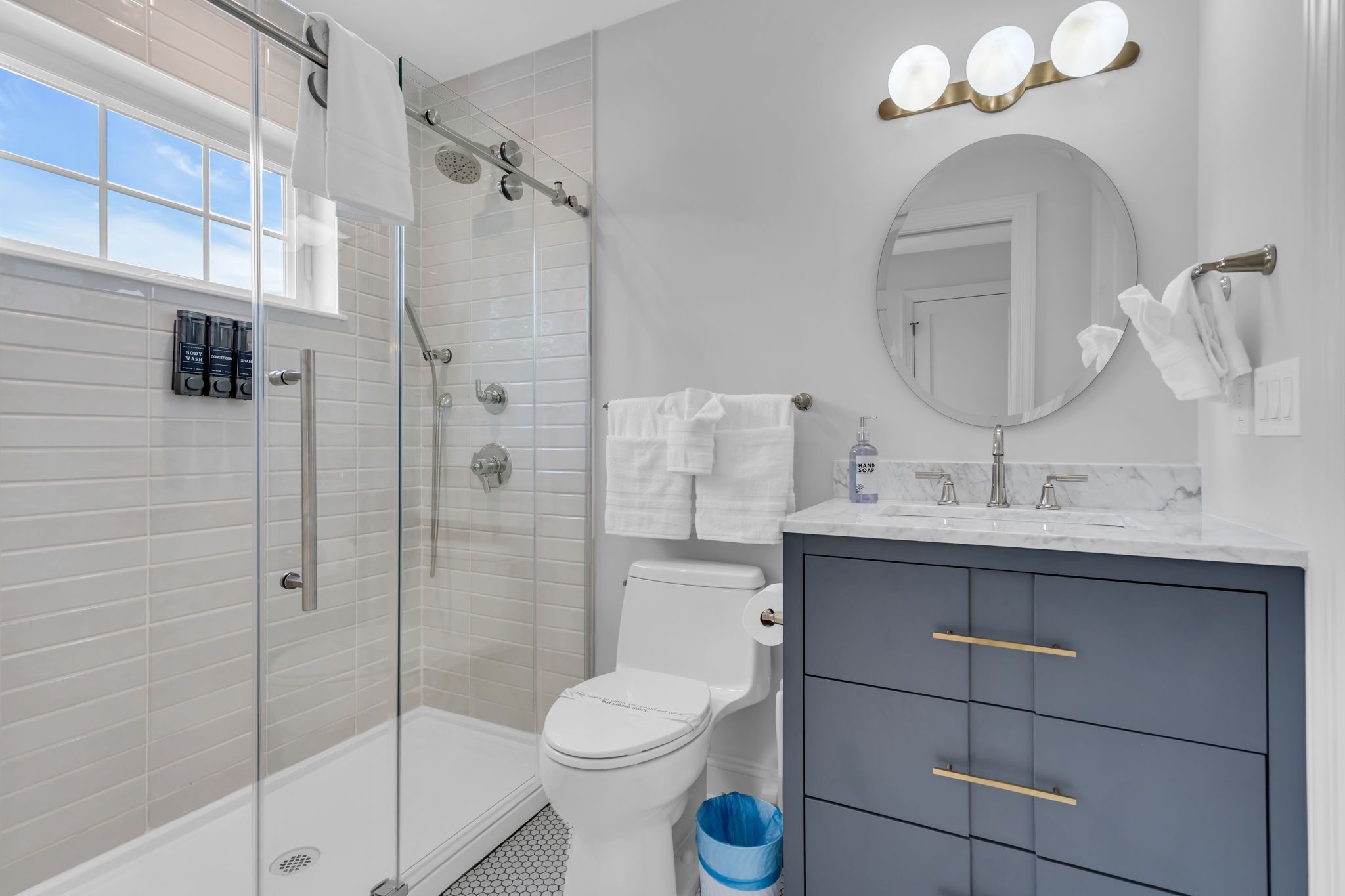 A modern bathroom with a glass-enclosed shower, a toilet, a vanity with drawers, and a mirror with lights.
