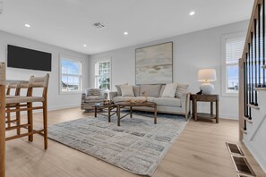 Una sala de estar moderna con sofá, mesa de centro y sillones, un televisor de pantalla plana y un amplio ventanal.