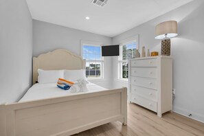 Un dormitorio con cama, cómoda, televisor y ventana.