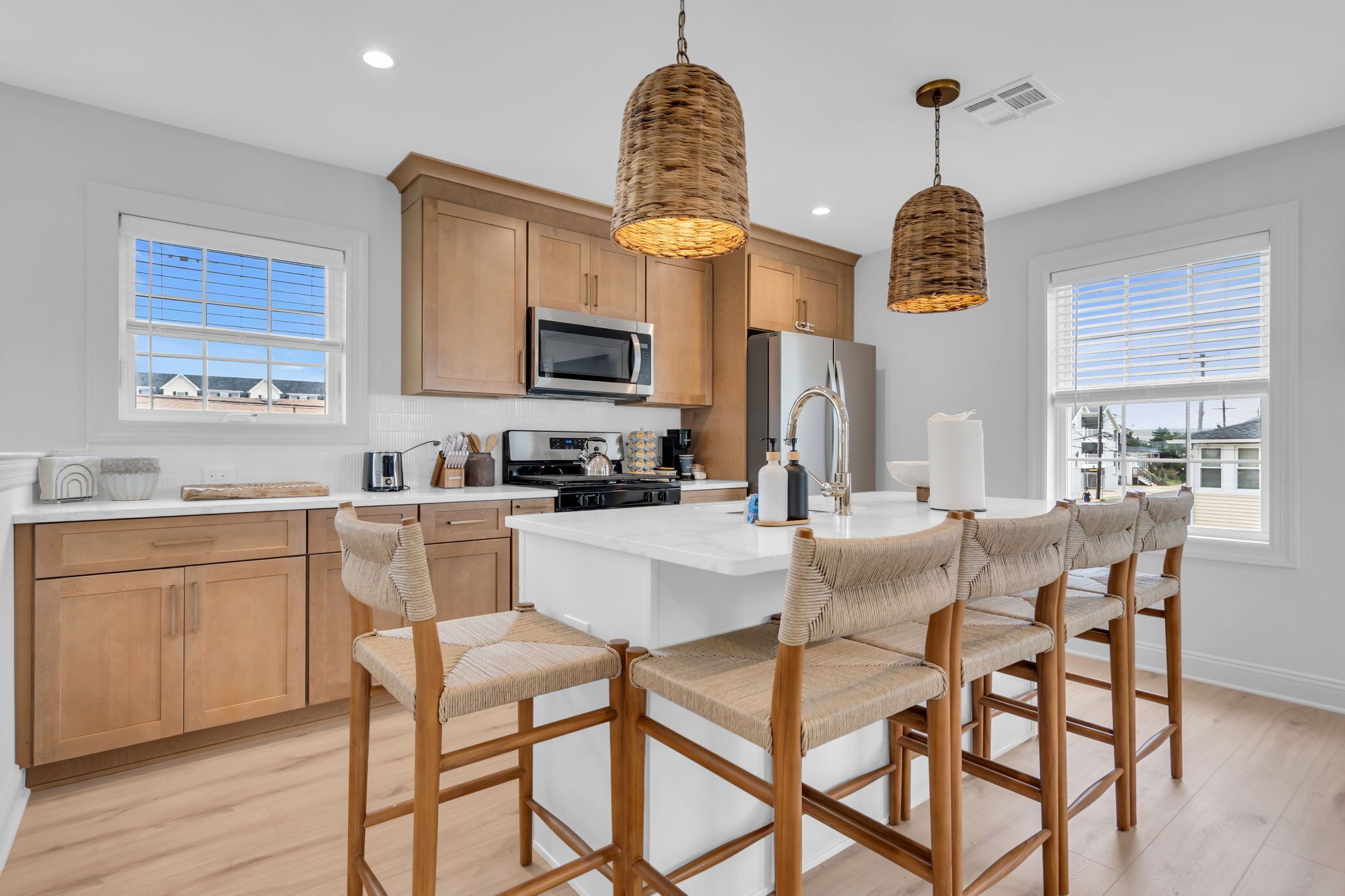 A modern kitchen with wooden cabinets, a central island with bar stools, and two hanging wicker pendant lights.