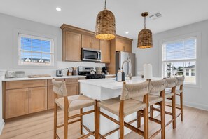 Una cocina moderna con gabinetes de madera, una isla central con taburetes de bar y dos lámparas colgantes de mimbre.