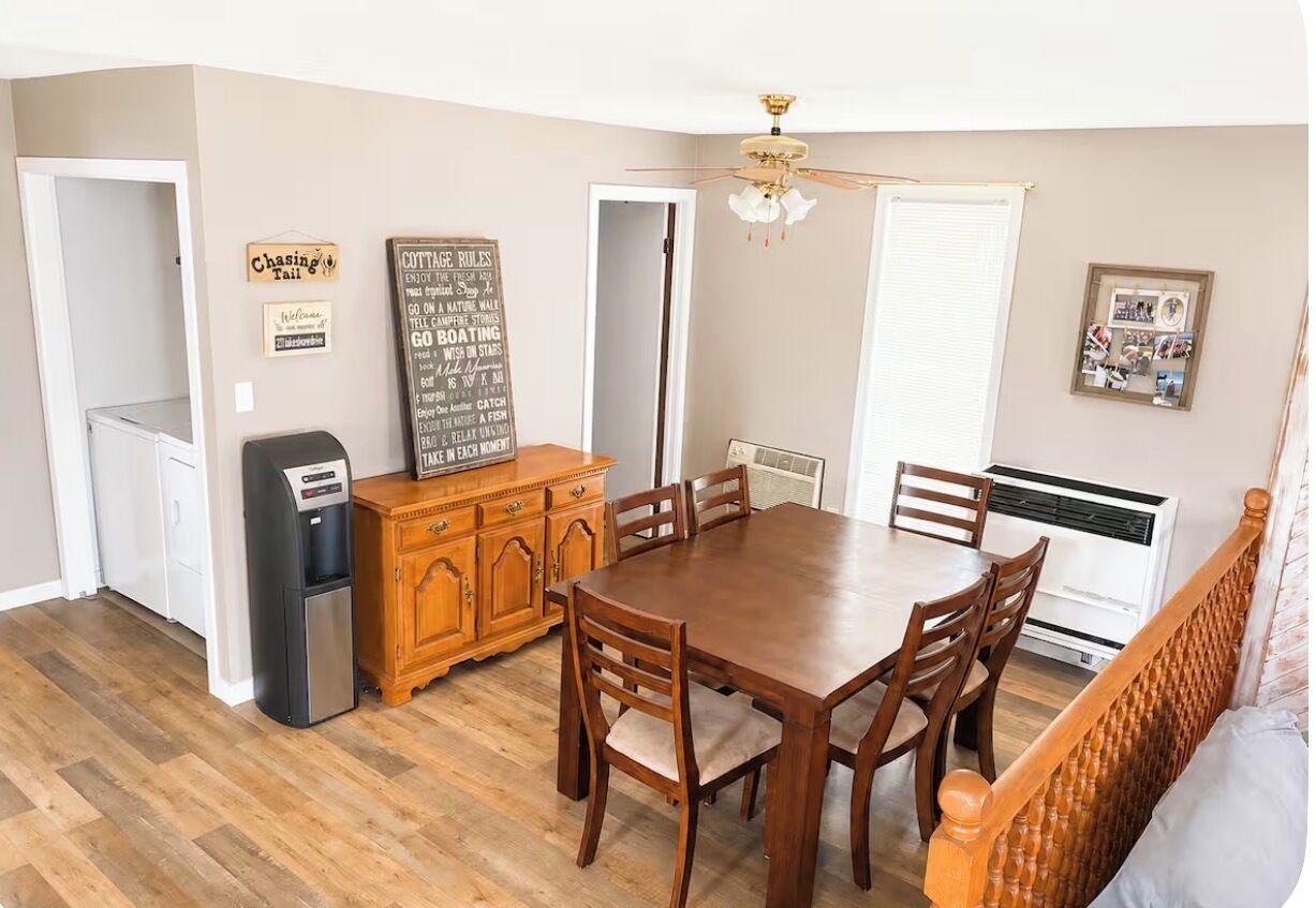 A dining area with a wooden table and chairs, a refrigerator, a wooden cabinet, and a ceiling fan.