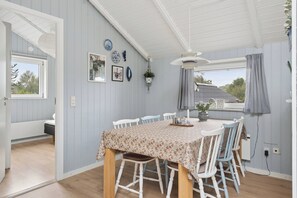 A dining area with a table set for four, surrounded by chairs, with a view of the outdoors through a window. - Lovely, well-designed holiday home for 6 (Hejls)