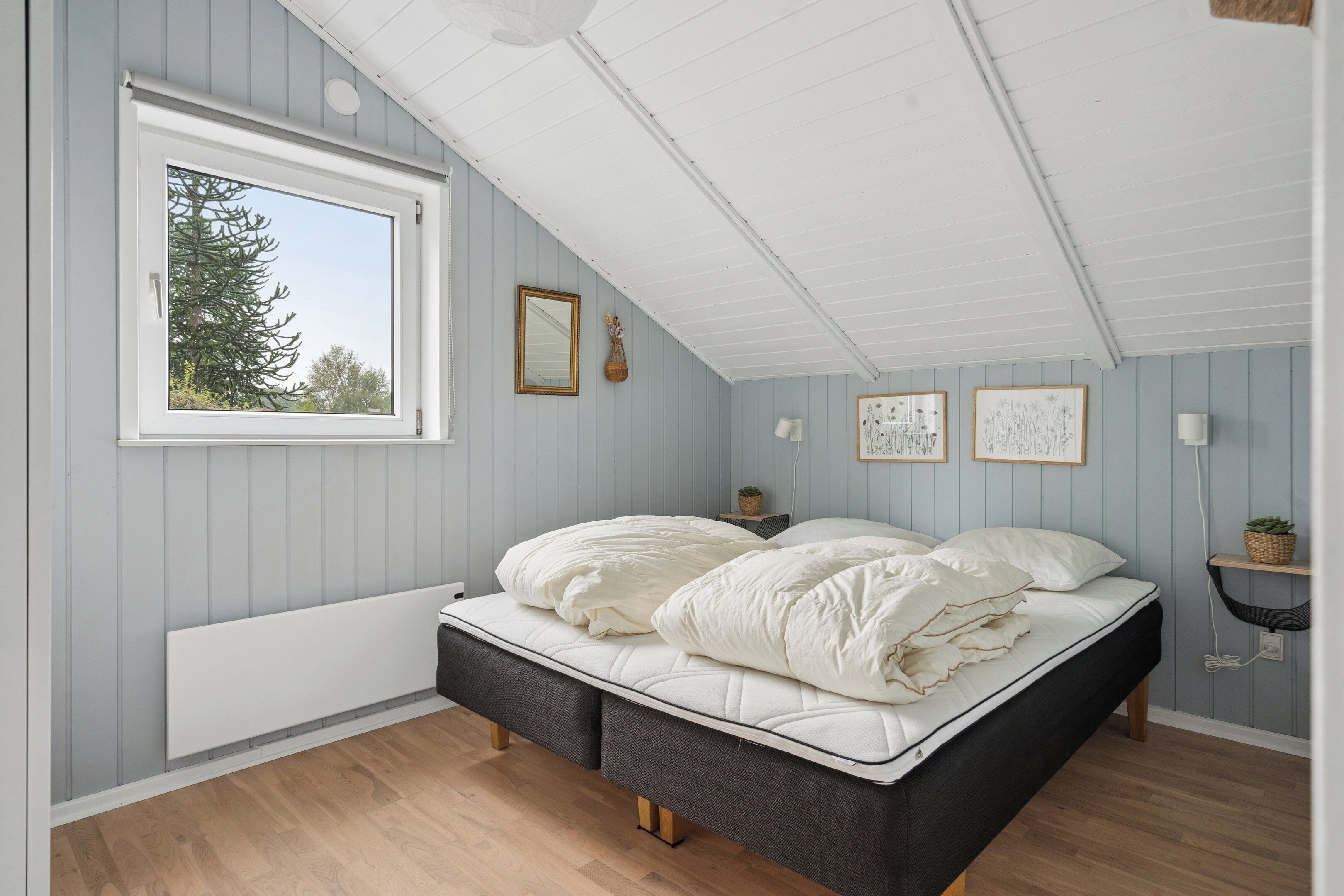 Un dormitorio con cama, ventana, espejo montado en la pared e impresiones botánicas enmarcadas.