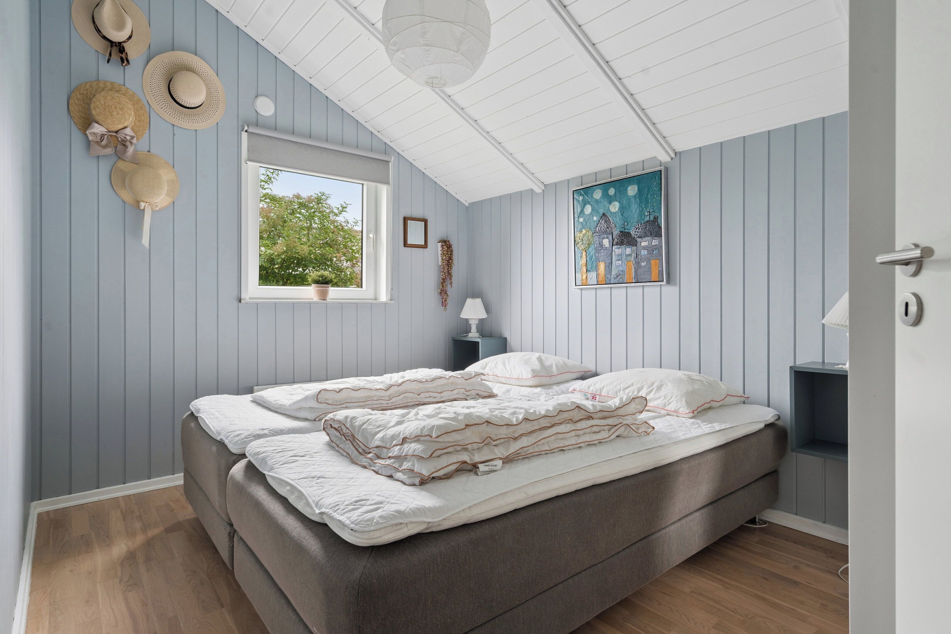 A bedroom with a bed, a window, a wall-mounted lamp, and a painting.