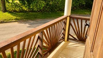Un balcon en bois avec une balustrade ornée, un sol carrelé et une vue sur une route et la verdure.