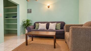 Una sala de estar con un sofá, una mesa de centro, una planta en maceta y un aplique de pared.
