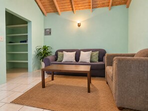 Una sala de estar con un sofá, una mesa de centro, una planta en maceta y un aplique de pared.