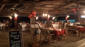Un espacio exterior para comer con mesas dispuestas para una comida, un cartel que anuncia música en vivo y una pizarra de menú.