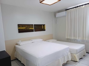 Ein Hotelzimmer mit zwei Betten, einer Wand-Klimaanlage und einem Fenster mit Vorhängen.