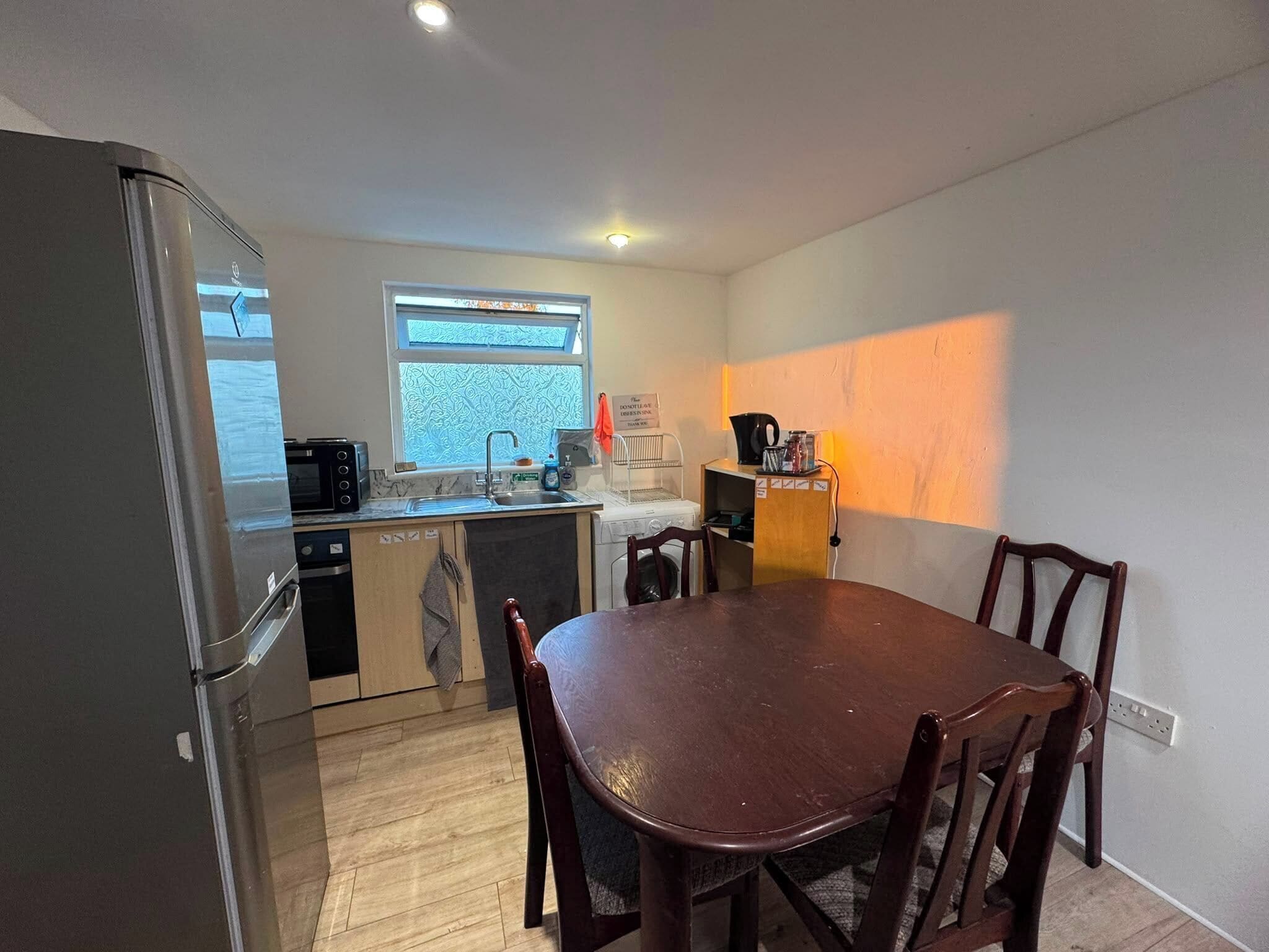 A compact kitchen with a refrigerator, microwave, sink, and a dining table with chairs.