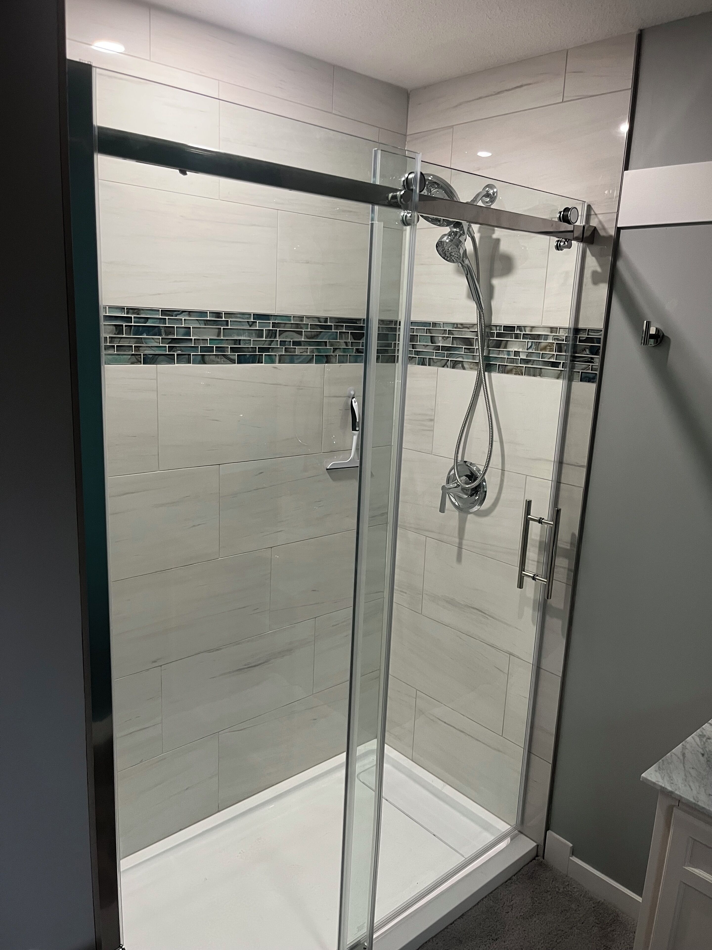 A modern shower enclosure with a glass door, a handheld showerhead, and a wall-mounted faucet.
