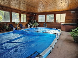 An indoor swimming pool with a wooden ceiling, surrounded by windows and potted plants.